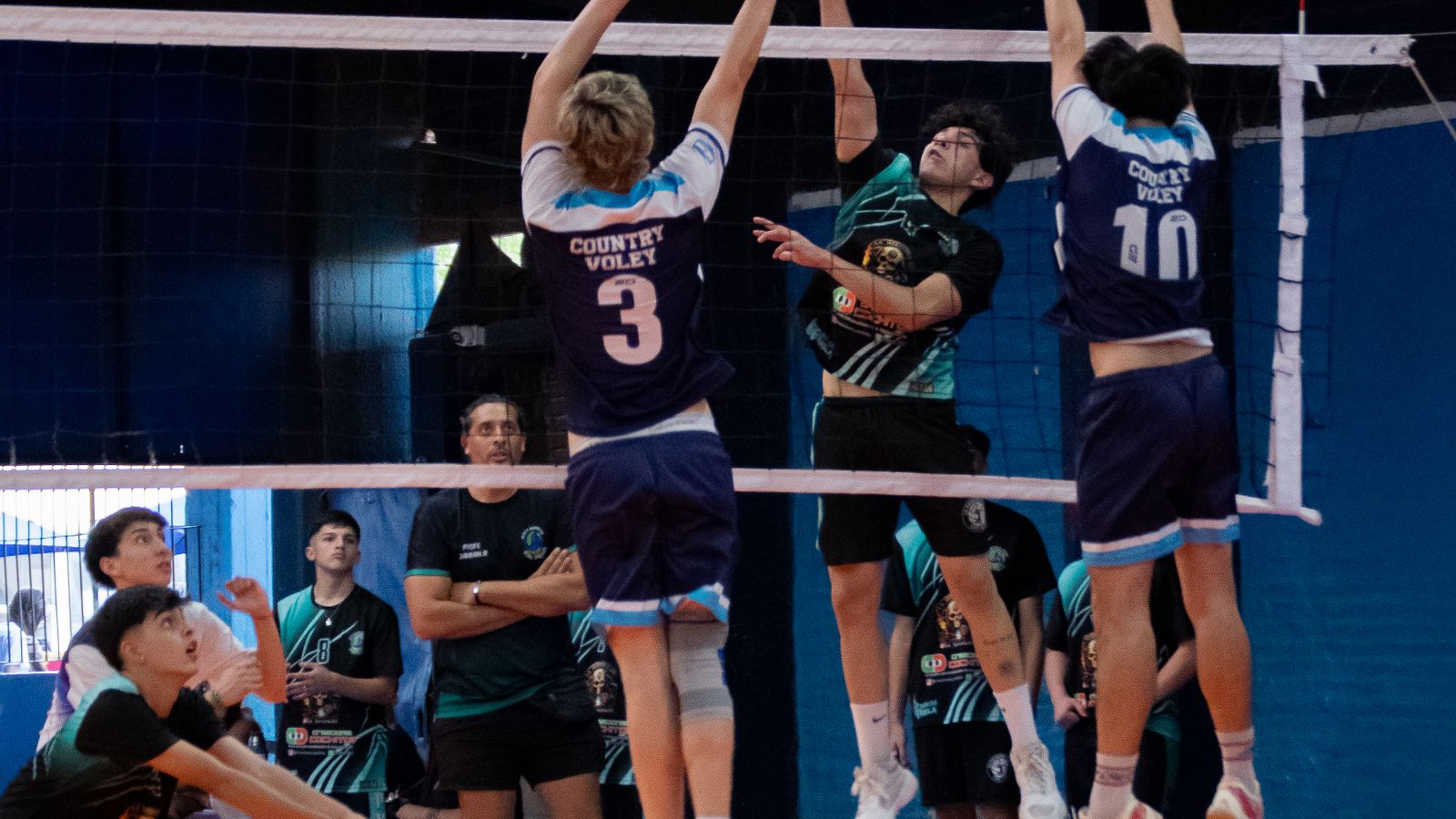 High school volleyball players competing at the net during an indoor match